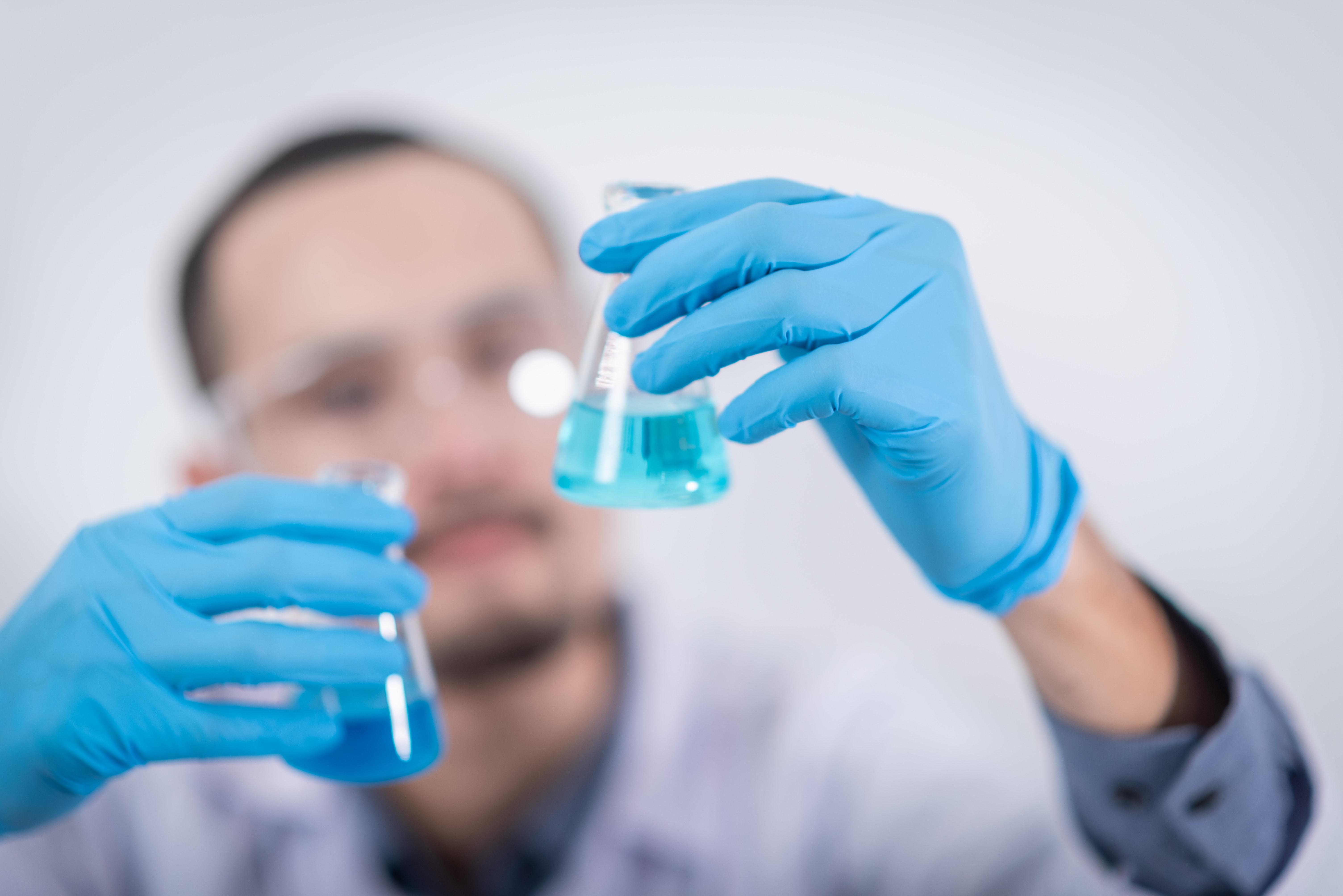 A chemist holding two flasks with chemicals inside of them